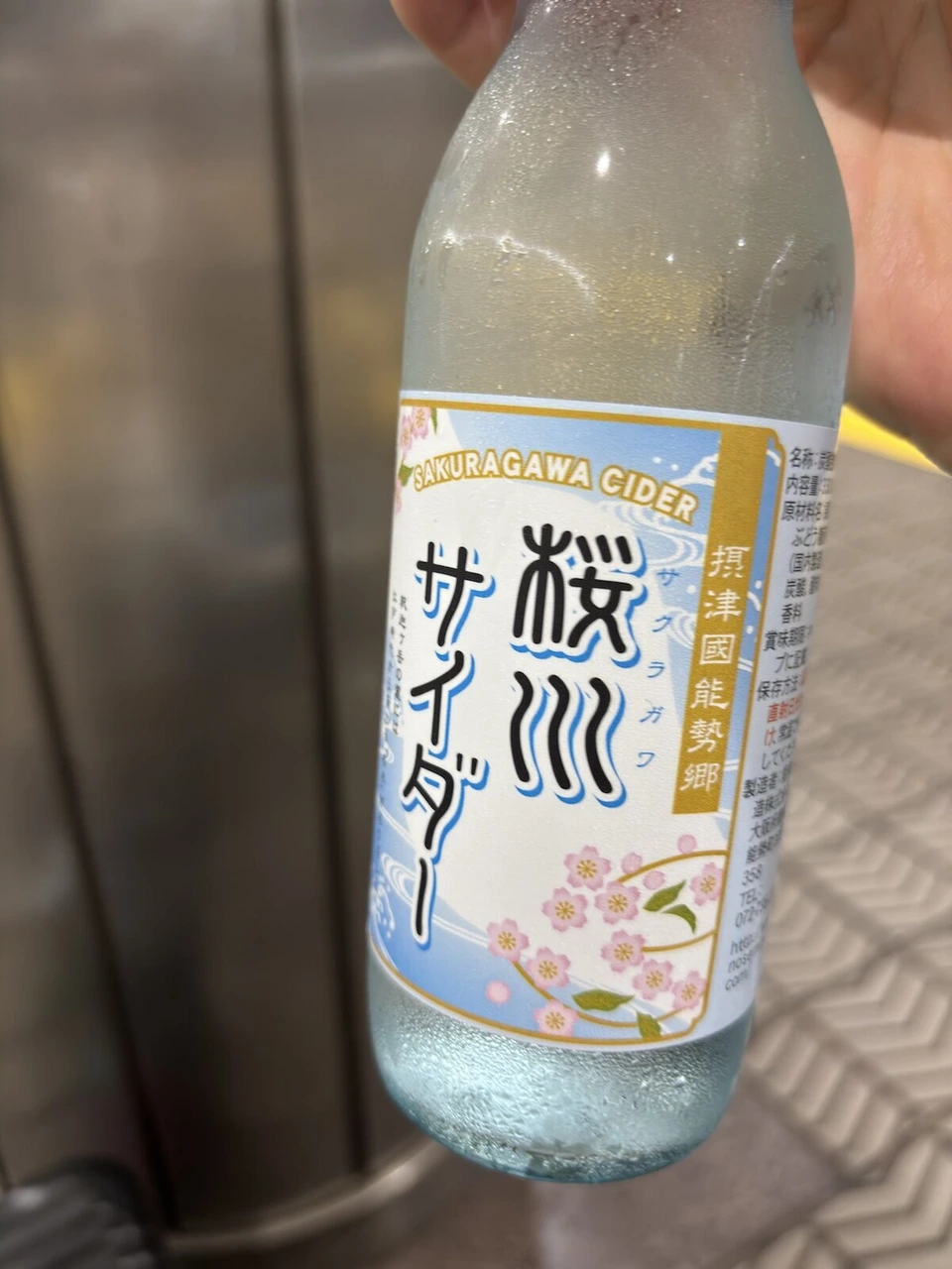 手に持った桜川サイダーの瓶。摂津国能勢郷と書かれたラベル