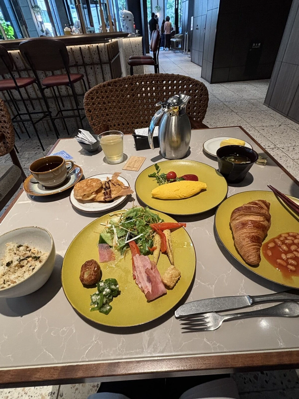 voco大阪セントラル1階LOKAL HOUSEの朝食のテーブル。黄色い皿にオムレツ、クロワッサンとベイクドビーンズ、サラダとベーコン、ご飯、味噌汁、コーヒー