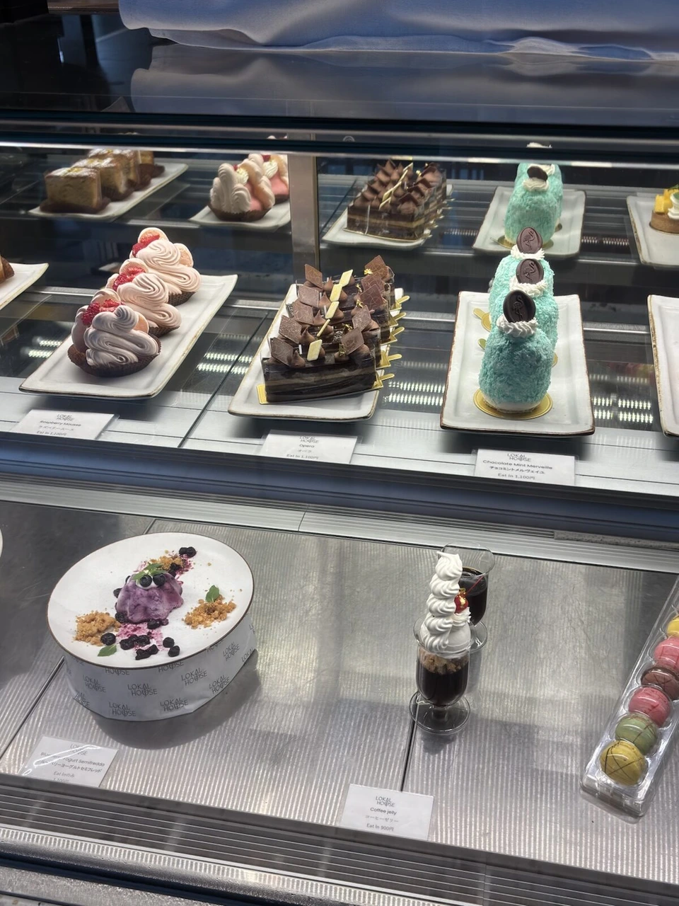 LOKAL HOUSEのショーケースに並ぶケーキ。ピンクのクリーム、チョコレート、水色のケーキ、紫のデザート、マカロン