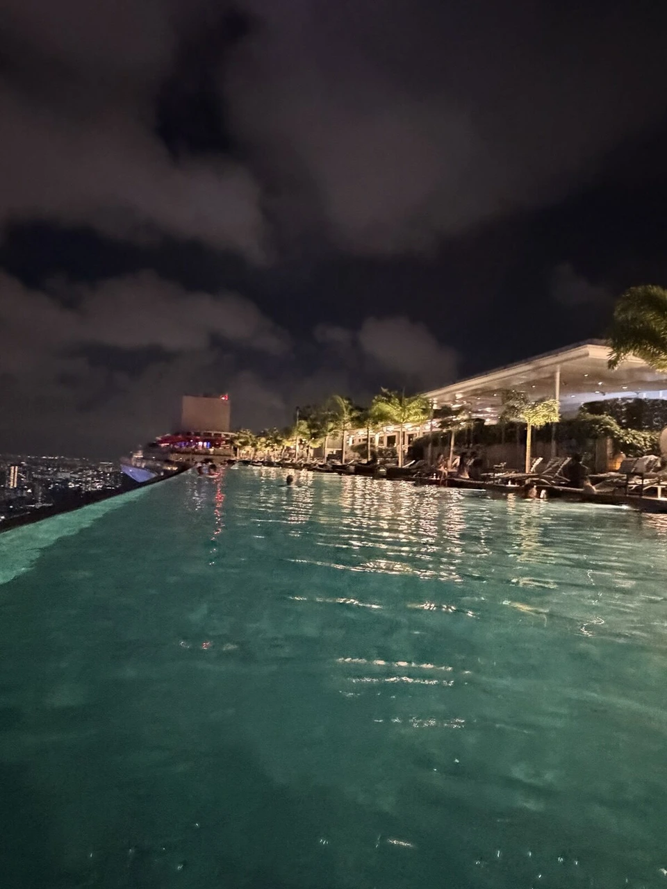 夜のマリーナベイ・サンズのインフィニティプール。緑に光る水面と、縁の向こうの夜景