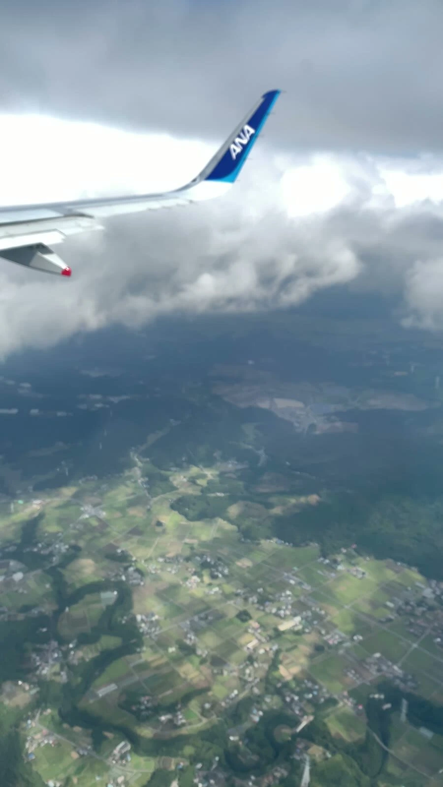 雲の下に出たNH22の機窓。主翼の向こうに田畑と山が広がる