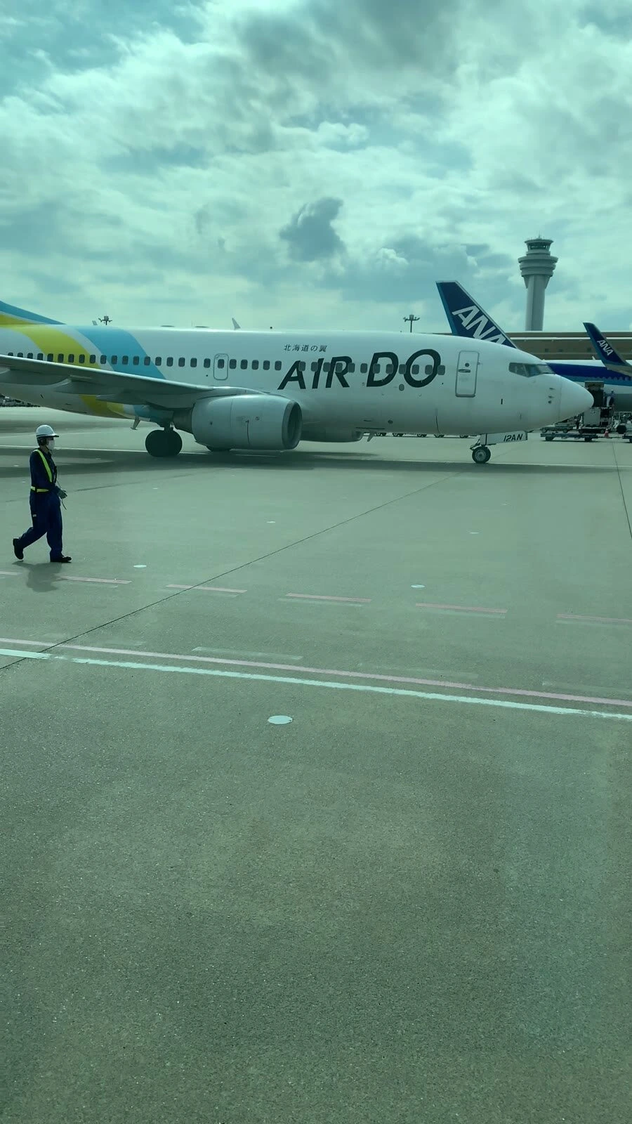 羽田空港の駐機場。AIRDOの737と、奥に管制塔とANA機の尾翼、手前を歩く作業員