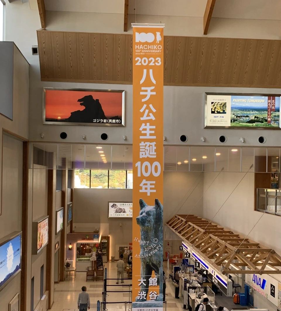 大館能代空港のターミナルの吹き抜け。ハチ公生誕100年のオレンジ色の垂れ幕と、下の階のANAのカウンター