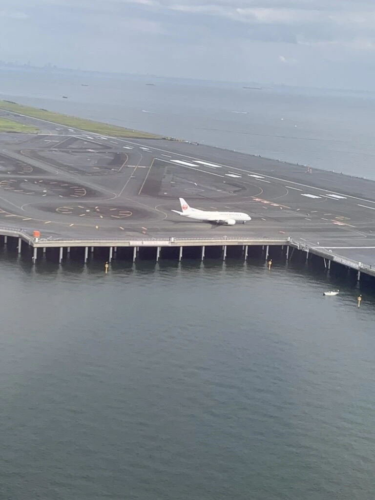 ANA NH22で羽田空港に着陸する前の機窓。海の上に張り出した滑走路と、地上を走るJAL機