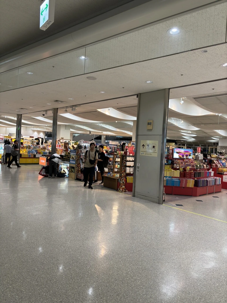 夜の那覇空港の明るい通路と、右側に並ぶ土産物の売店