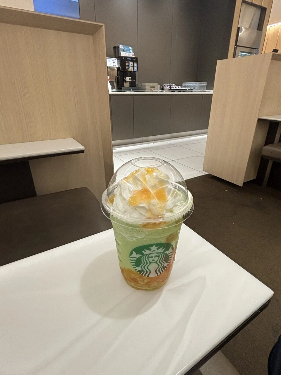 那覇空港で、木の仕切りのある席に置いたスターバックスのフラペチーノ