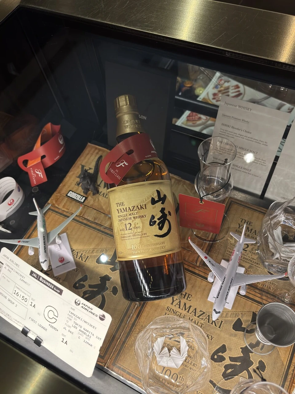 成田のJALラウンジのガラスケースに飾られた山崎12年のボトルと、飛行機の模型やグラス