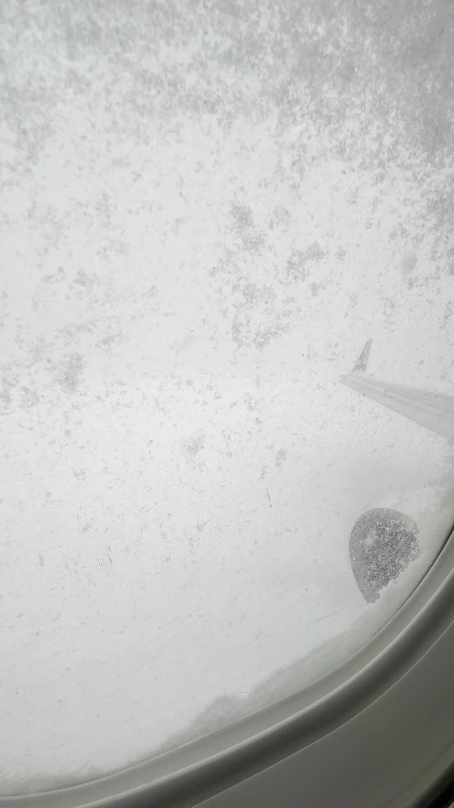 雪で真っ白になった機内の窓と、窓の端に見える主翼の先