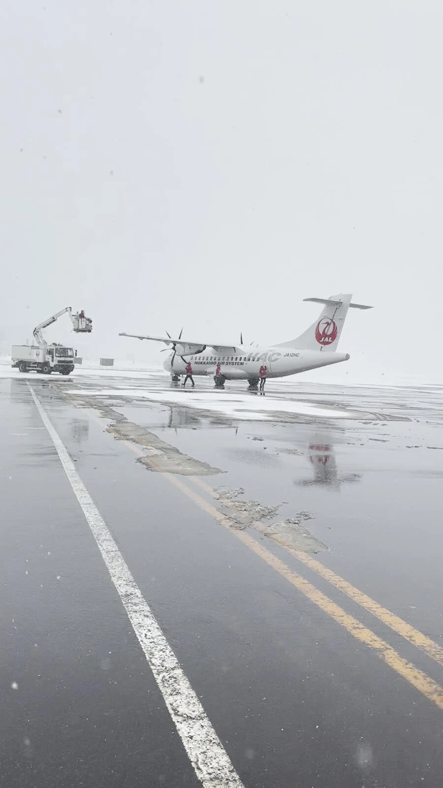 雪が降る丘珠空港の駐機場と、JALの尾翼のプロペラ機