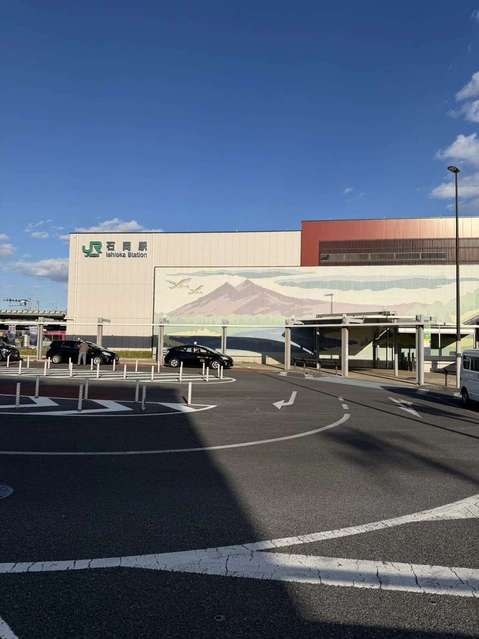 青空の下のJR石岡駅。駅舎の壁に筑波山と鳥のモザイク画