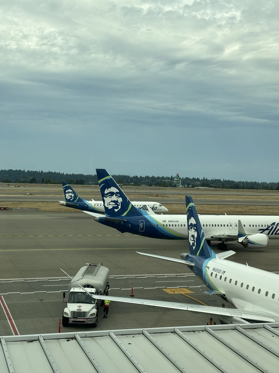 曇り空のシアトル空港。駐機場に並ぶアラスカ航空の機体と給油車