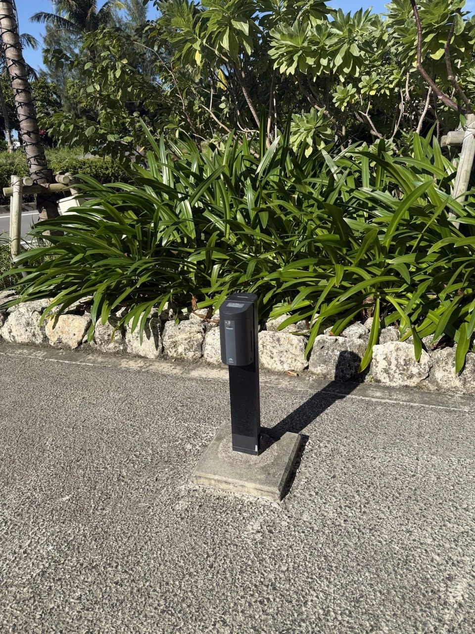 沖縄プリンスホテル オーシャンビューぎのわんの駐車場で、植え込みの前に立つ黒い普通充電器