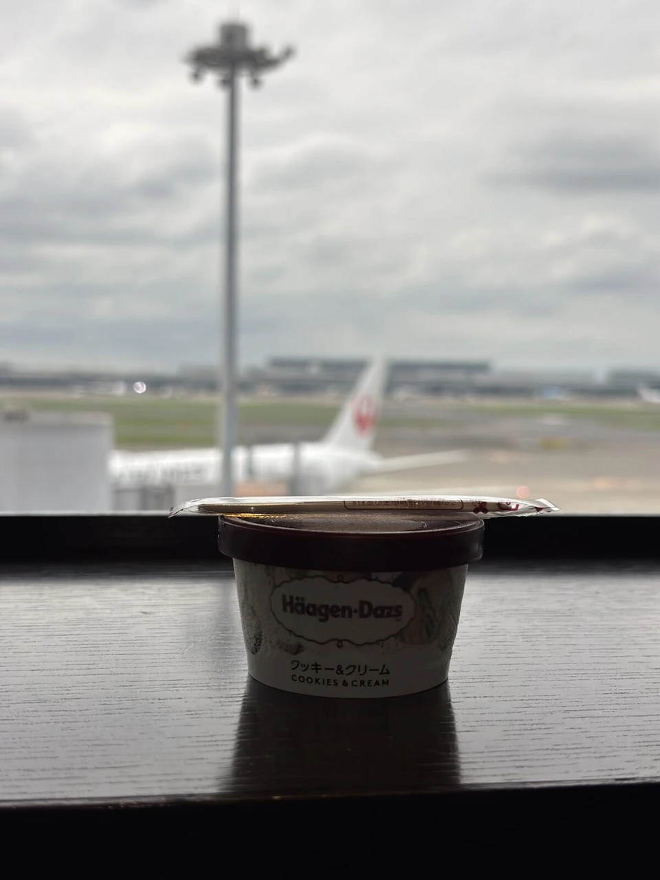 羽田のJALラウンジの窓際に置いたハーゲンダッツのクッキー&クリーム。窓の外にJAL機