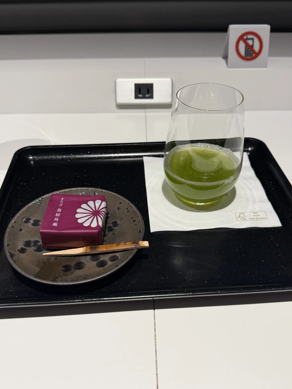 黒いトレーにのった緑茶のグラスと、紫の包みの和菓子