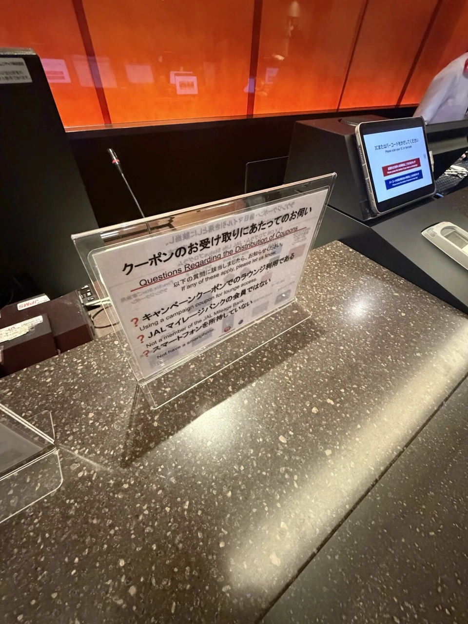 羽田空港のJALラウンジ受付。クーポン受け取りについての案内板とバーコードの読み取り機