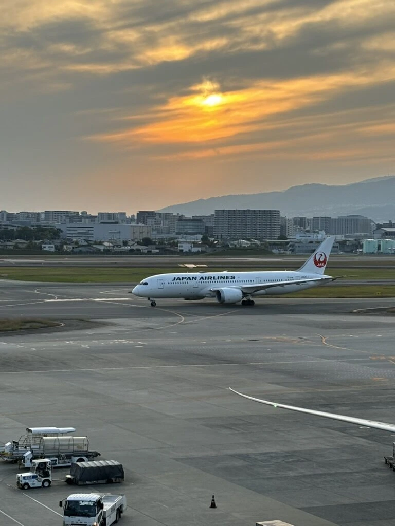 夕焼けの伊丹空港を走るJALの飛行機と、奥の山並み