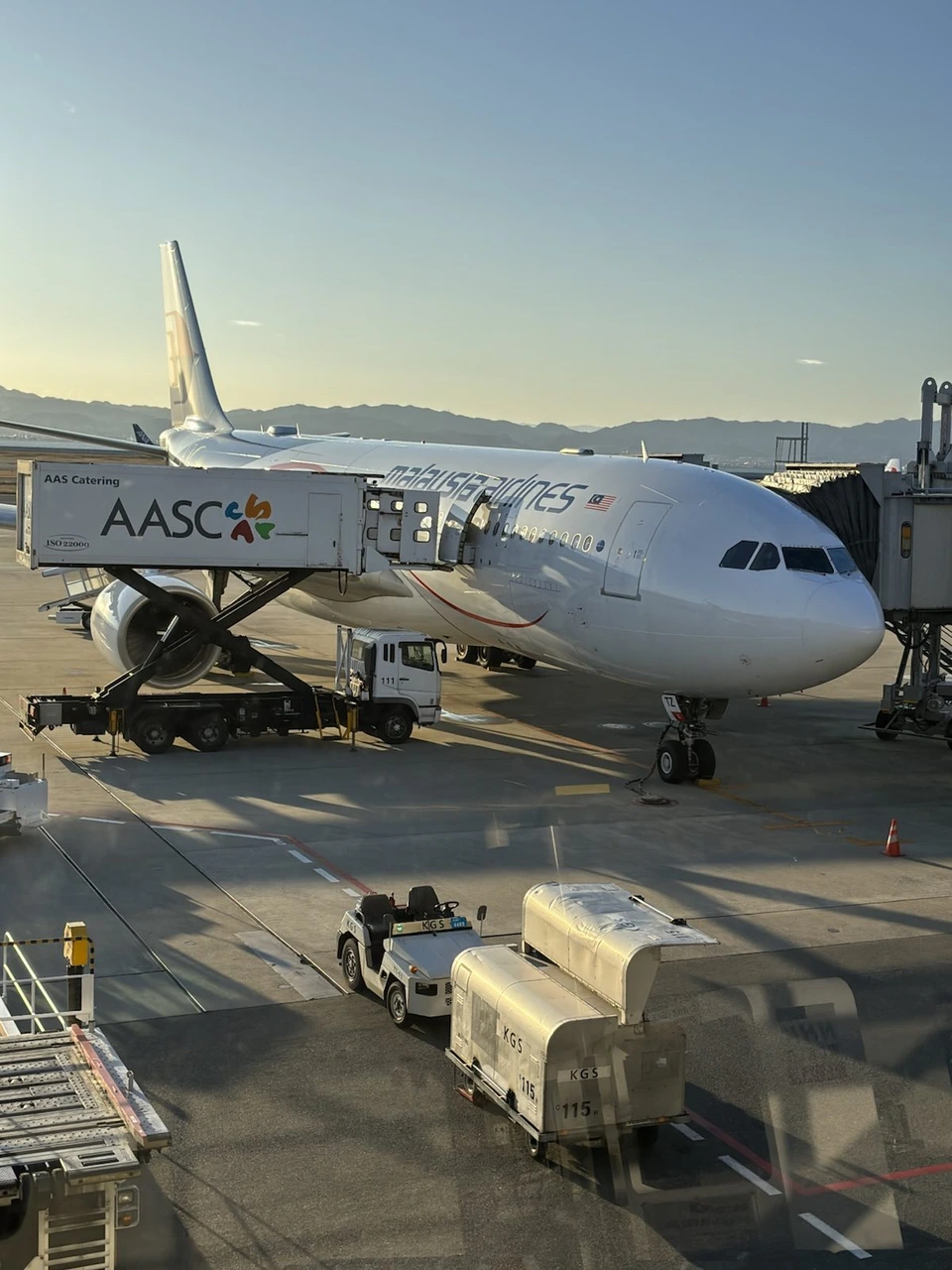 朝日の当たる関空の駐機場に止まるマレーシア航空の白い機体と、手前の給油車