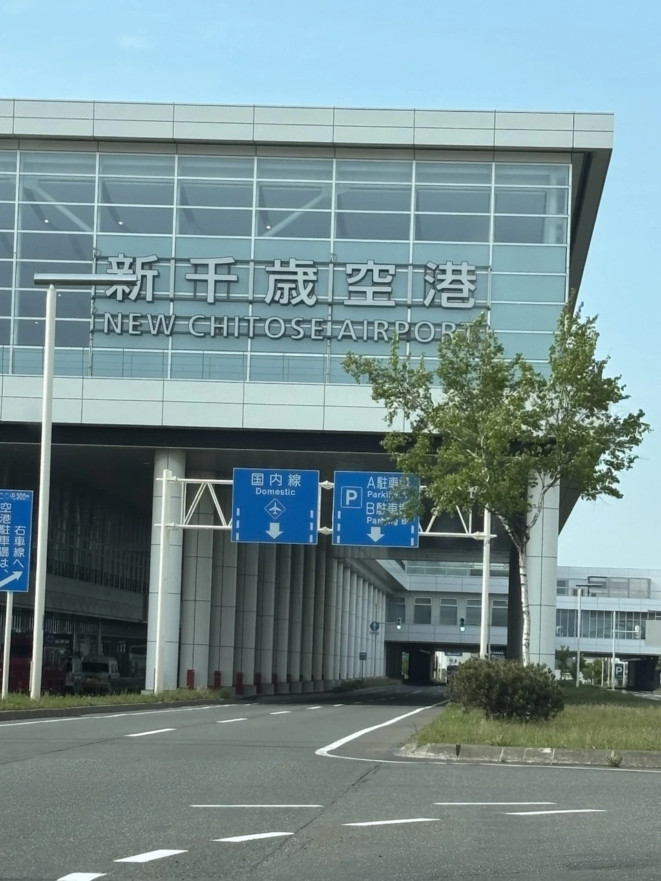「新千歳空港」の文字が入った旅客ターミナルビルの外観と、前の道路