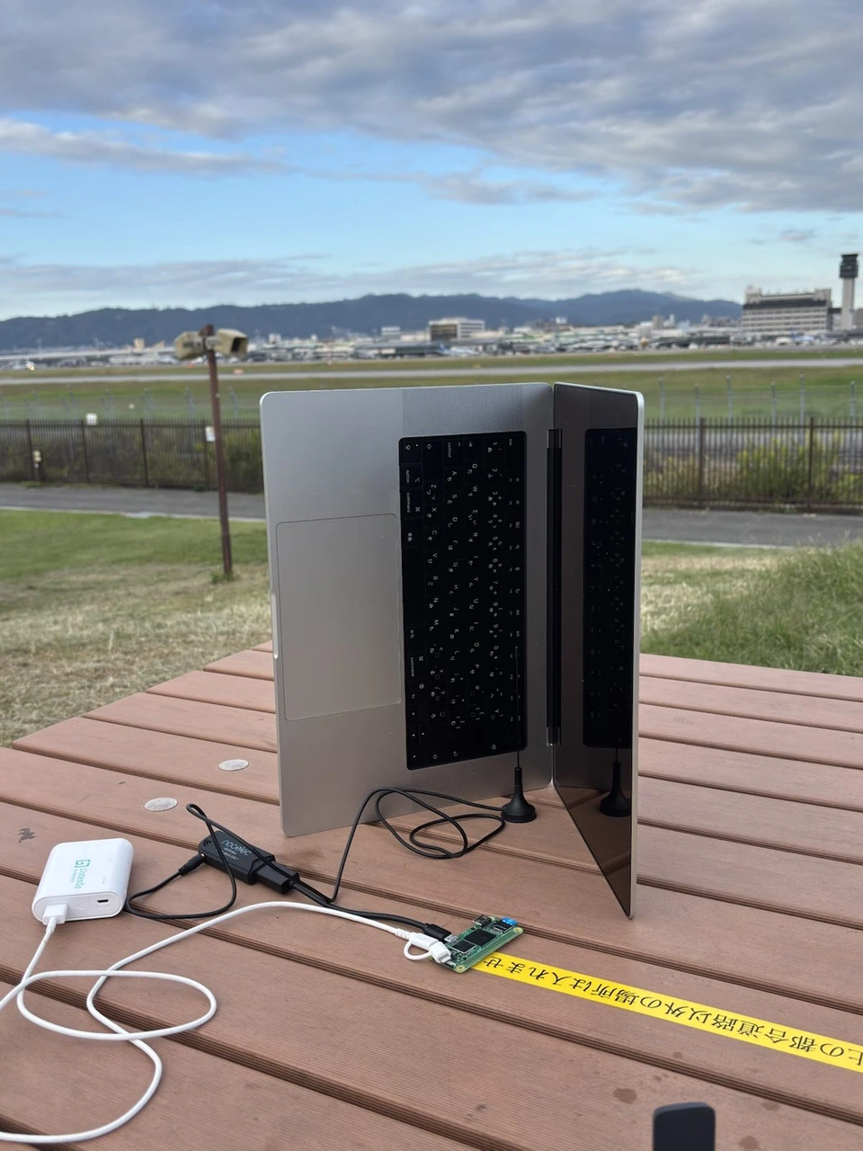 伊丹スカイパークのテーブルに立てたノートPCとラズパイ、受信機。奥に伊丹空港の滑走路と管制塔