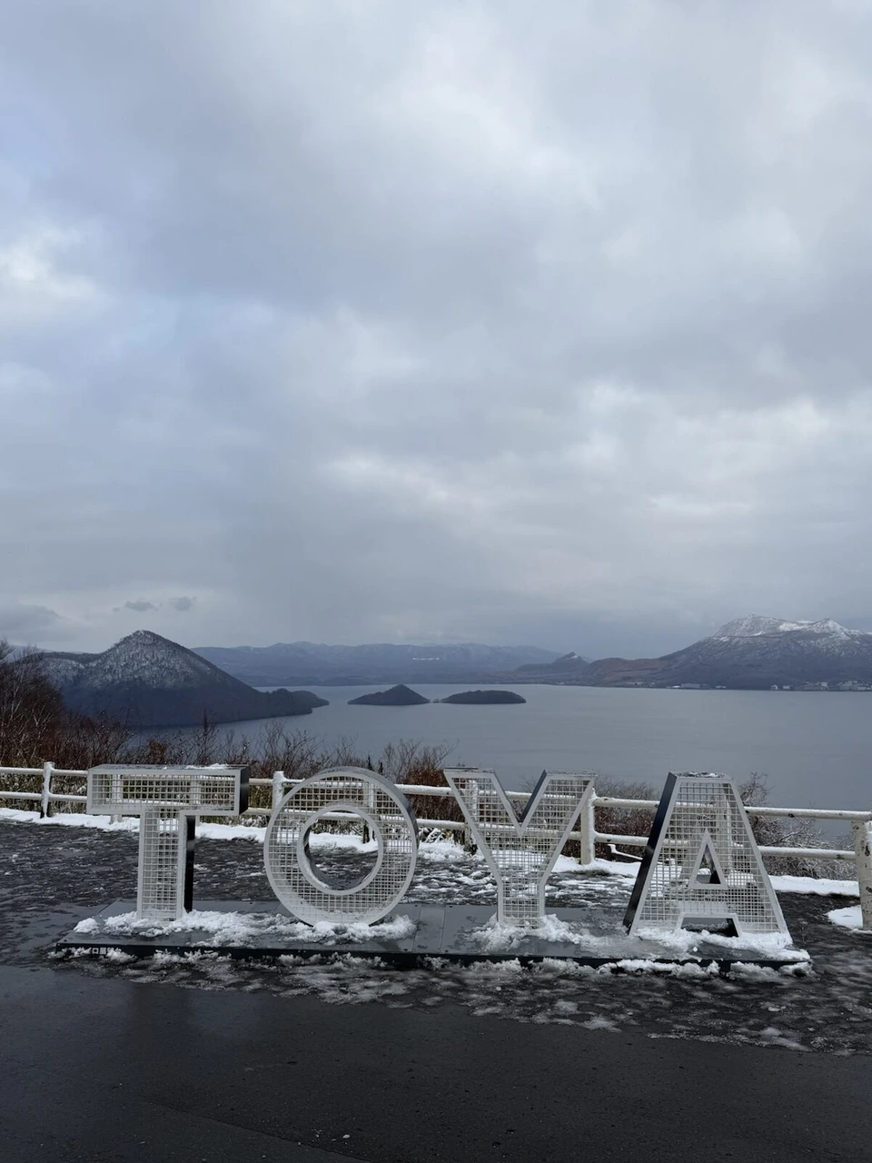 雪がうっすら積もったTOYAの文字のモニュメントと、曇り空の下の洞爺湖と中島