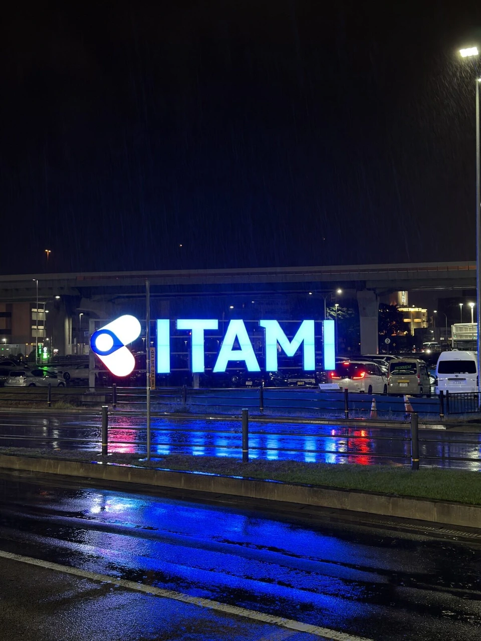 雨の夜の伊丹空港。青く光るITAMIの文字と、濡れた路面に映る青い光