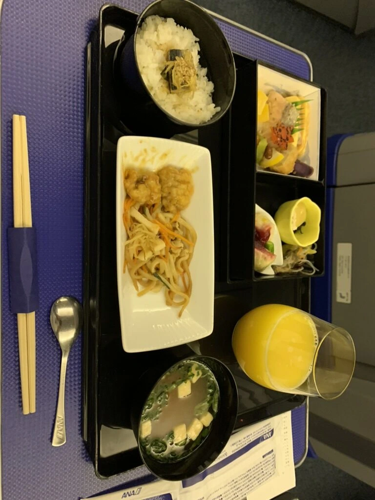 NH478 プレミアムクラスの機内食。揚げ物と麺の皿、ご飯、味噌汁、おかずの詰め合わせ
