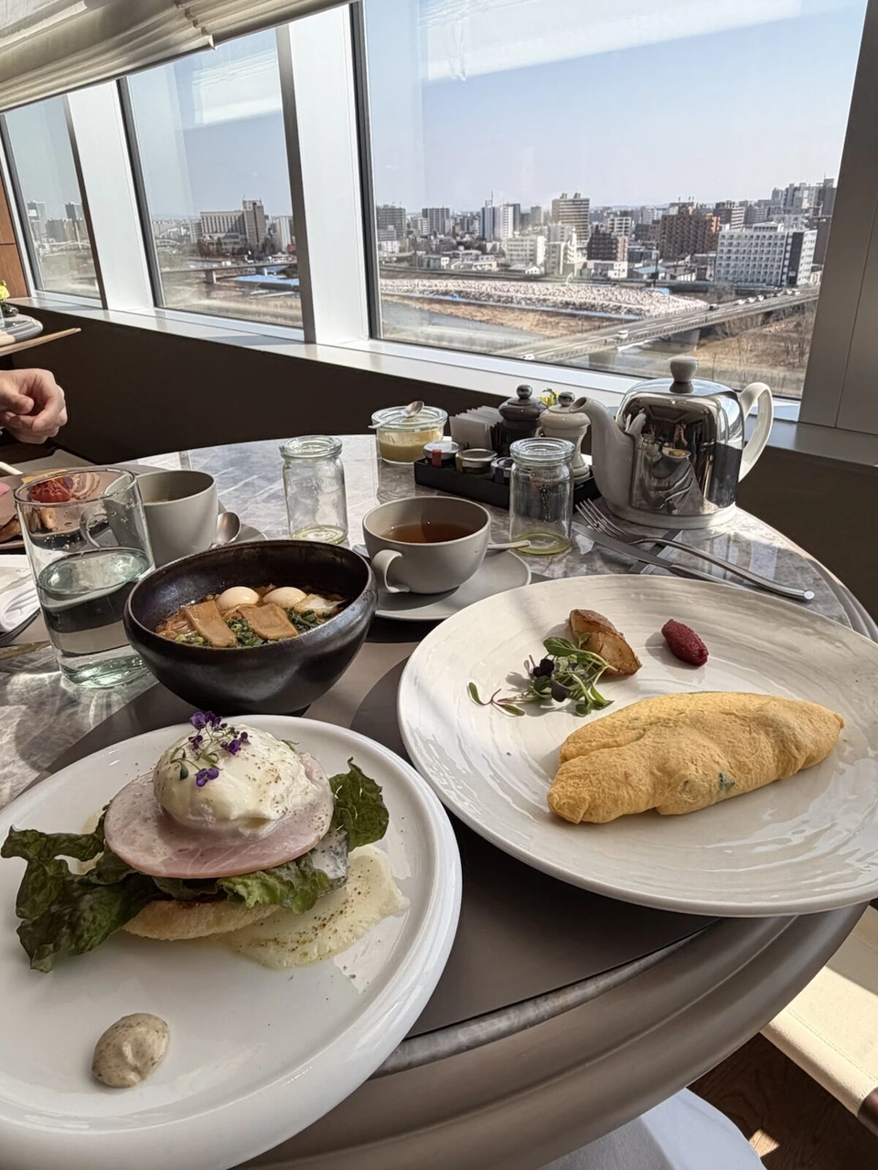 インターコンチネンタル札幌の朝食。エッグベネディクト、オムレツ、小鉢、紅茶のポット。窓の外に豊平川