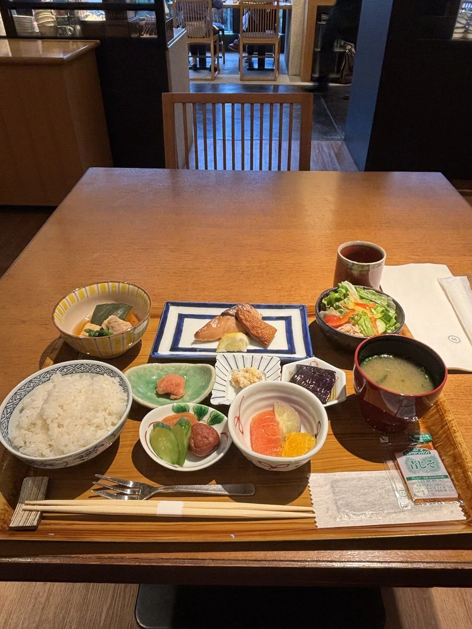 木のテーブルに並んだ朝食。ごはん、味噌汁、小鉢、サラダ