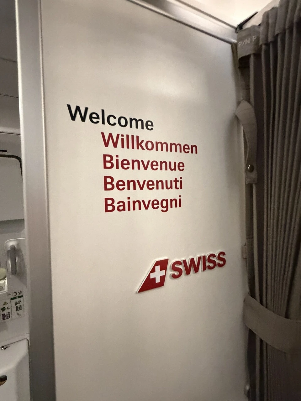 スイス航空の機内の入口の壁に、Welcome、Willkommen、Bienvenue、Benvenuti、Bainvegniの文字とSWISSのロゴ