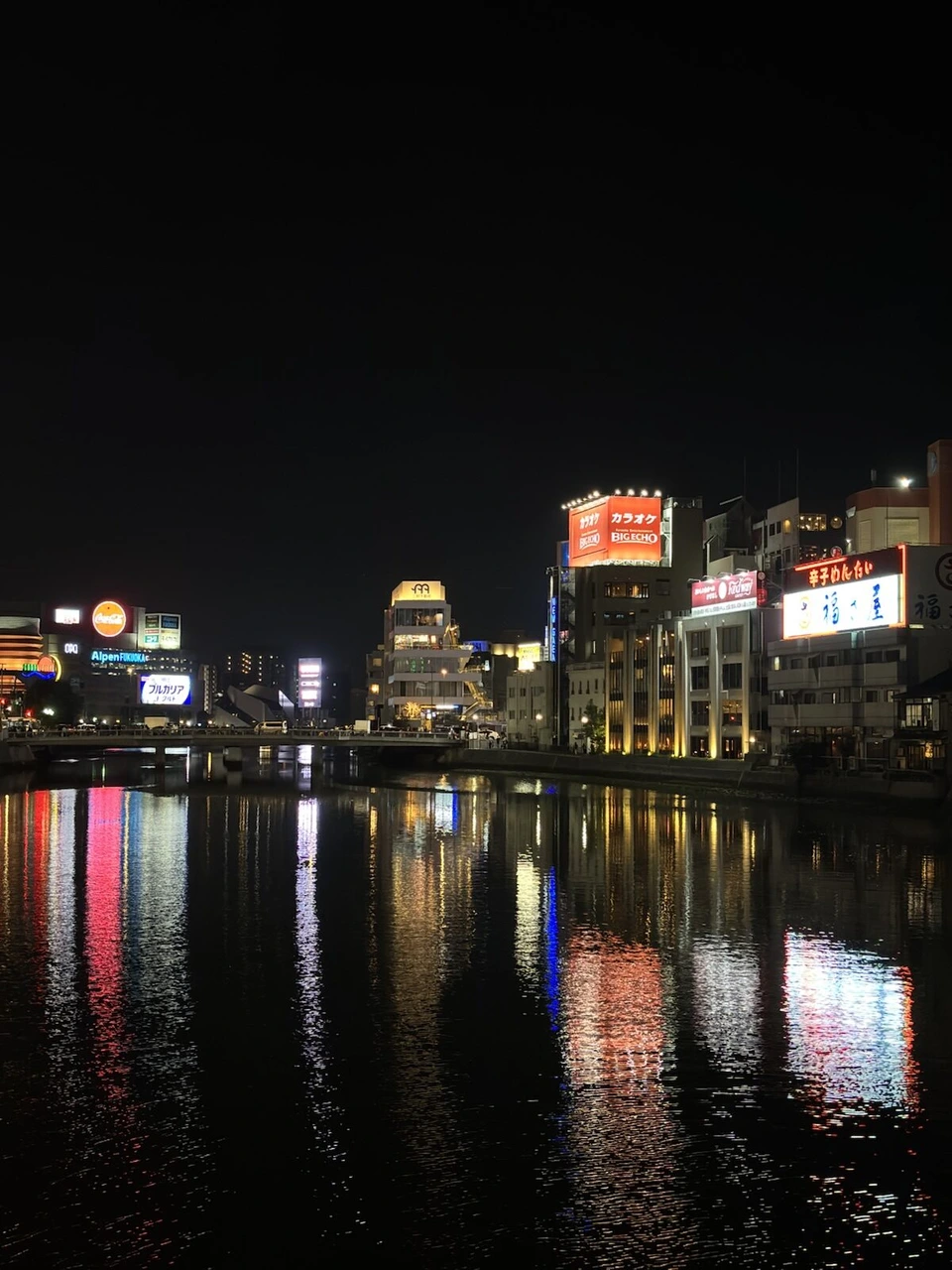 夜の那珂川に映る中洲のネオンと川沿いの建物