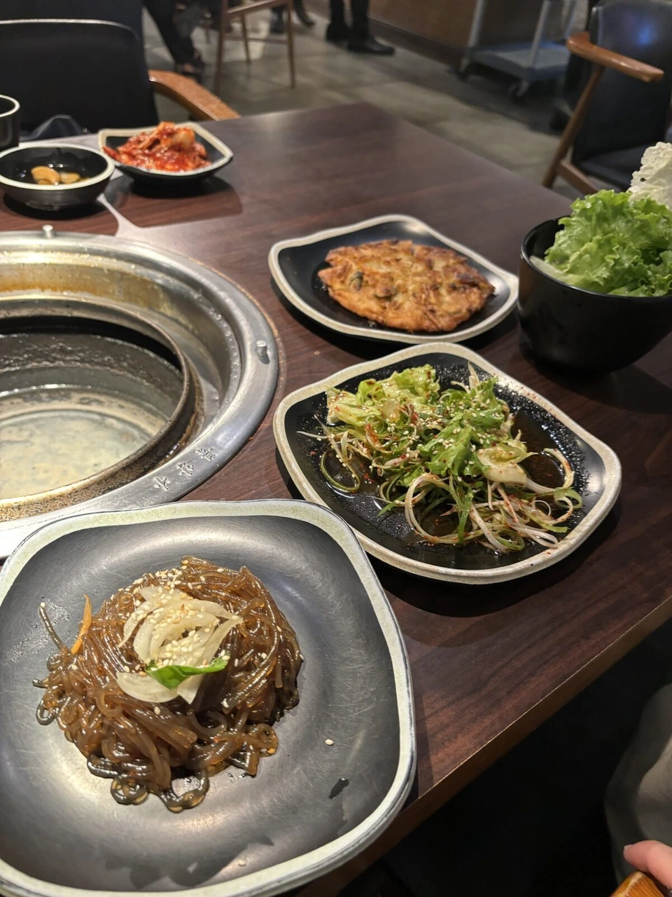 韓国焼肉店のテーブル。チャプチェとおかずの小皿、炭火のグリル