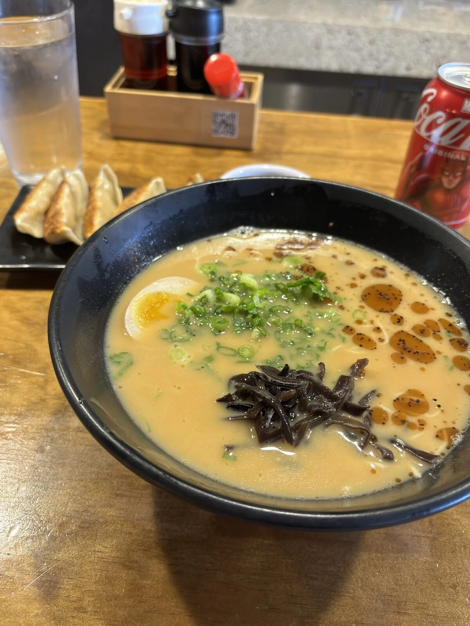 とんこつラーメンに半熟卵ときくらげ、横に餃子とコカ・コーラの缶
