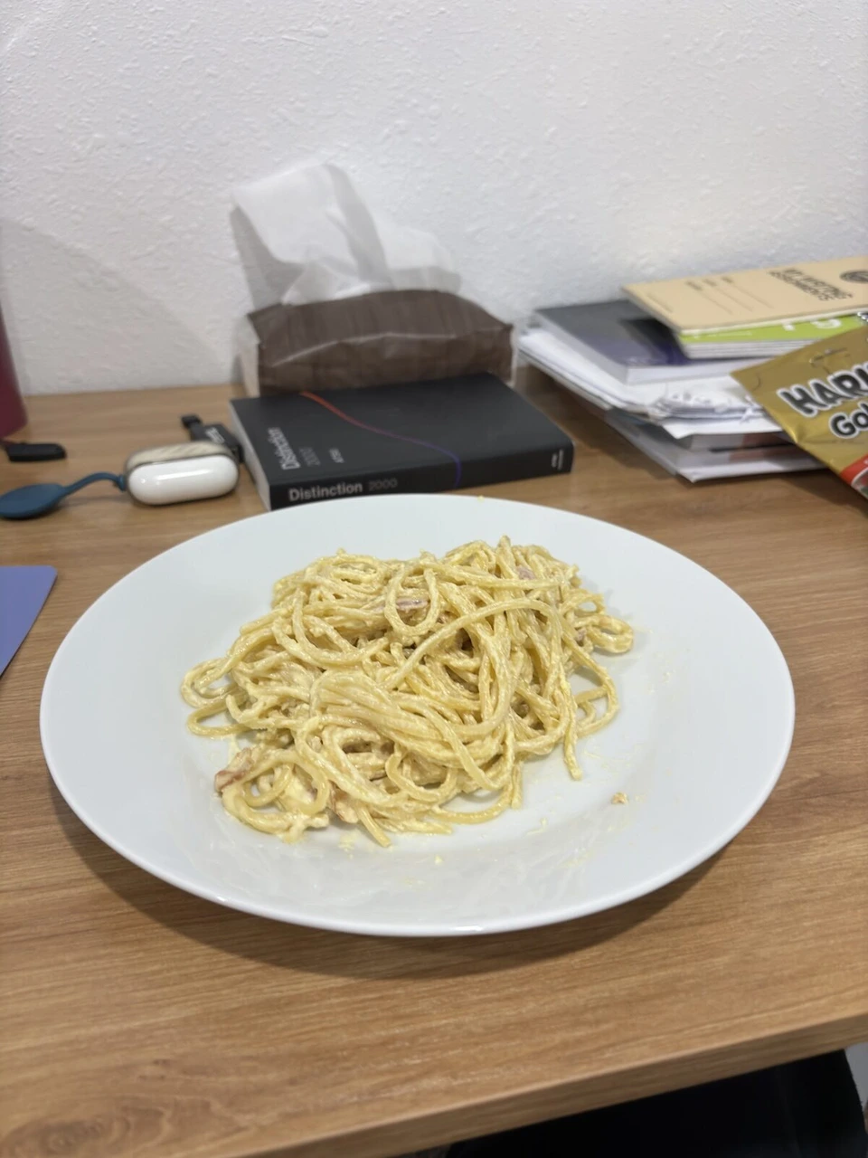 机の上に置いたクリームパスタの皿と、横の教科書