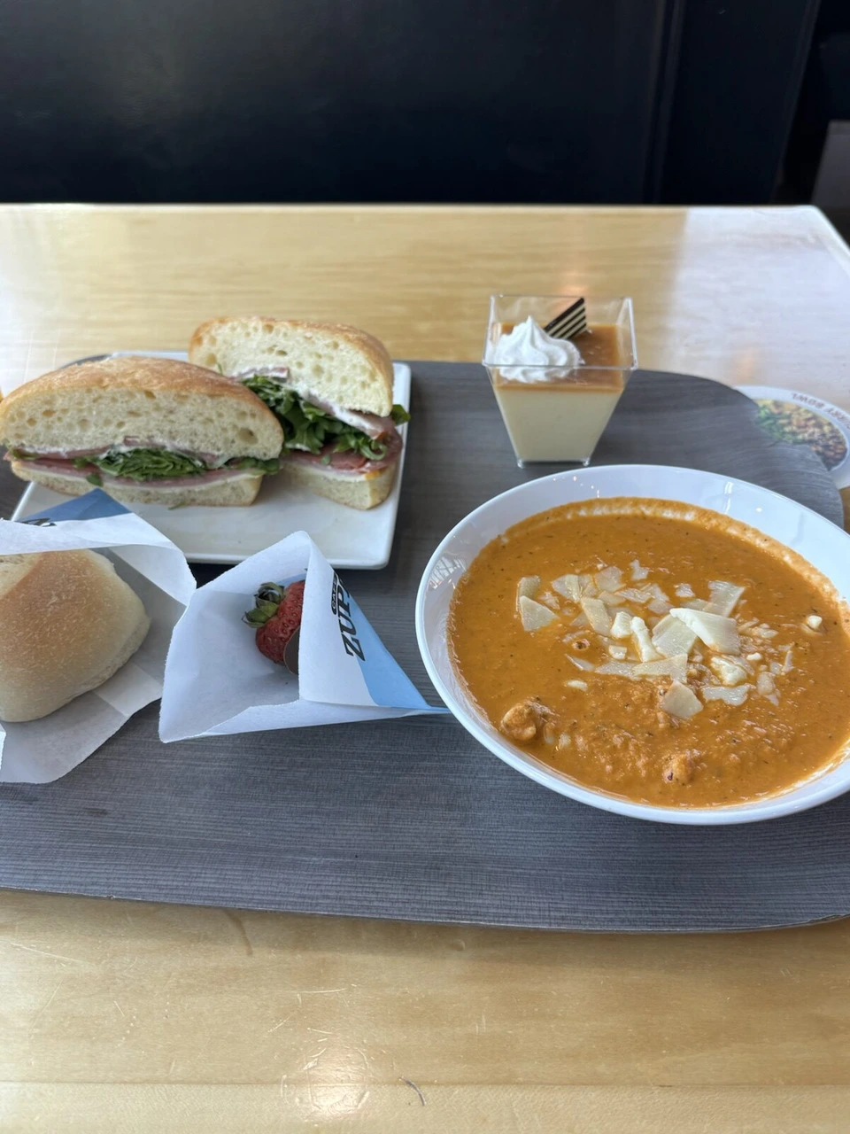 トレーにのったサンドイッチとトマトスープ、パン、小さなデザート