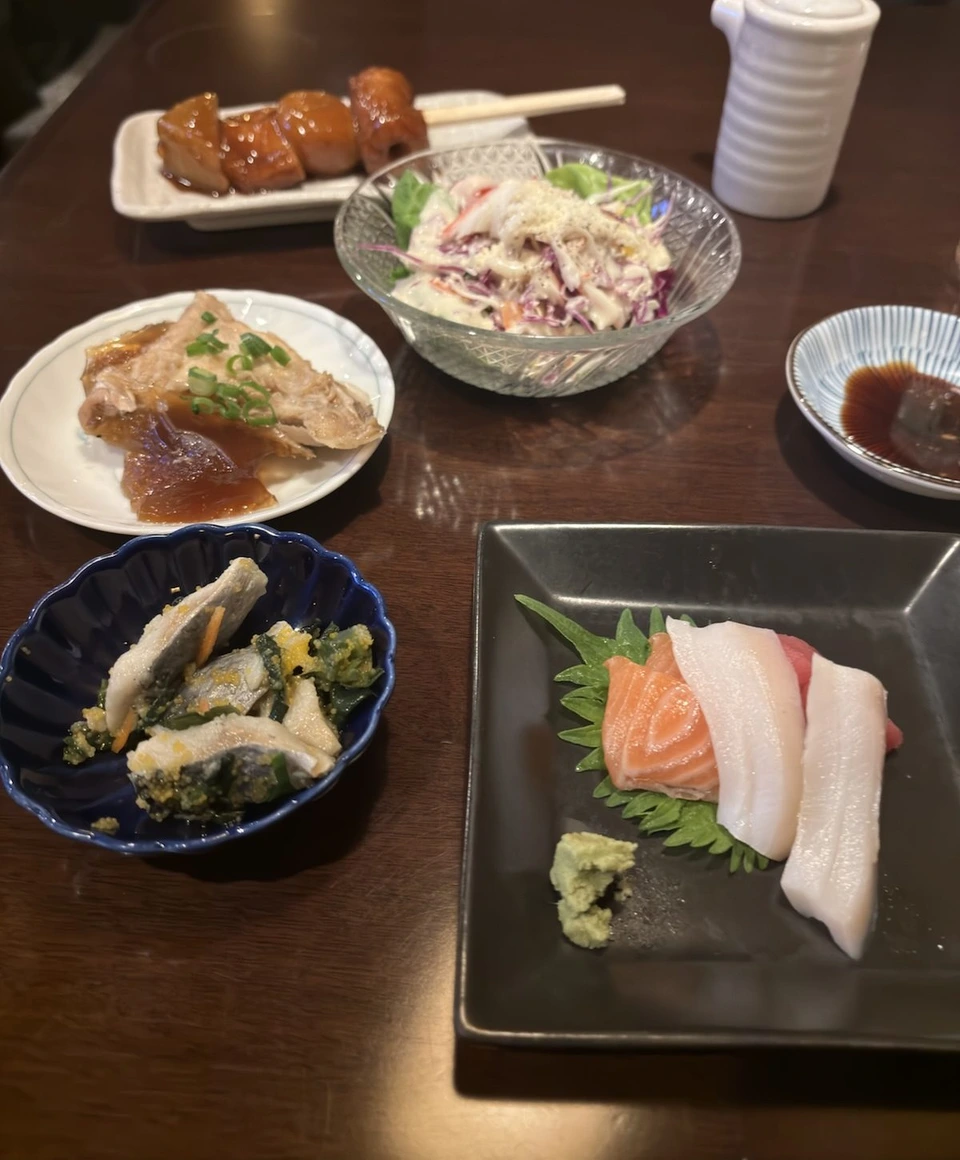 居酒屋のテーブル。たれの焼き鳥、コールスローのサラダ、魚の小鉢、サーモンと白身とマグロのお刺身の皿