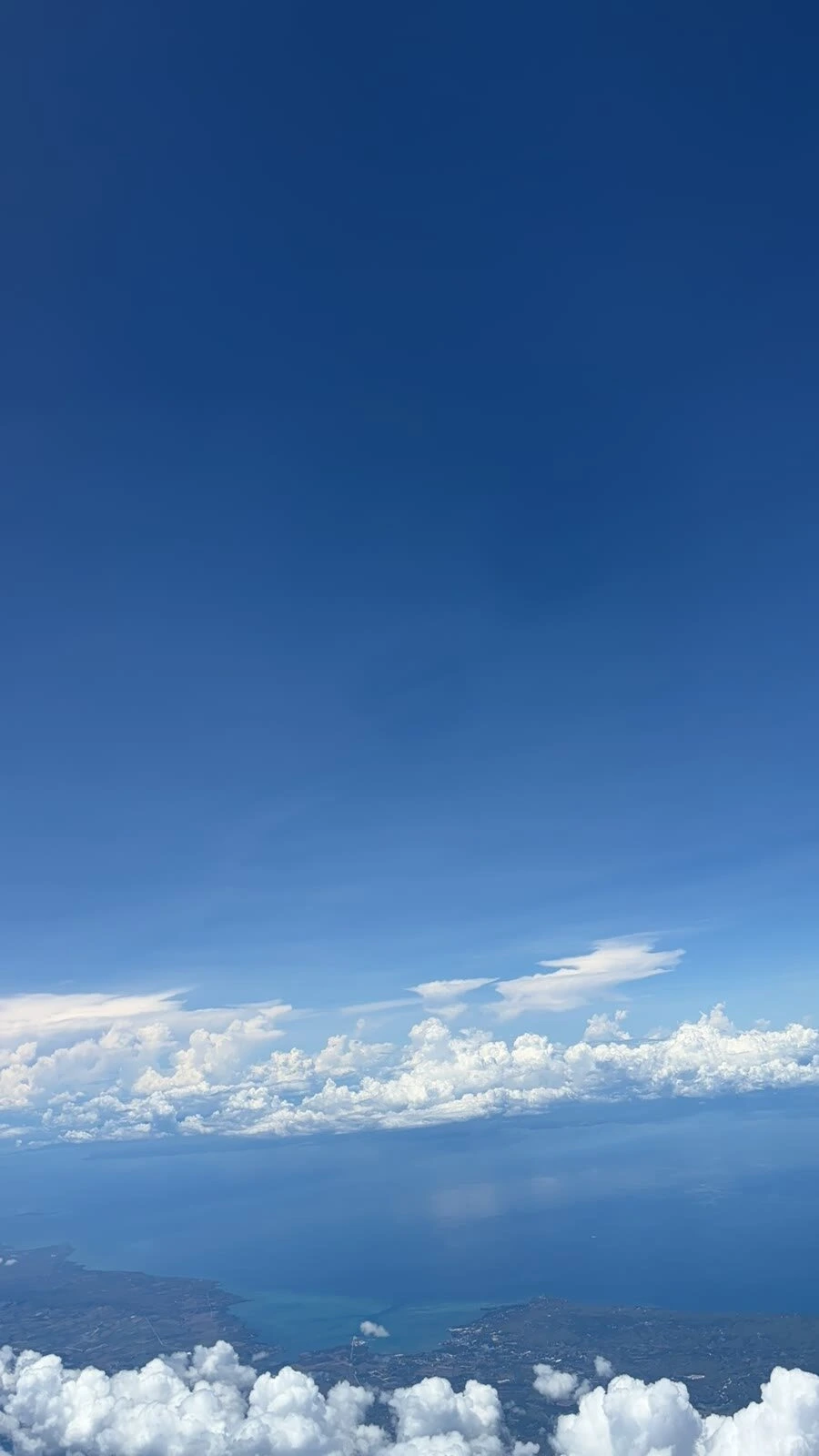 離陸後の機窓から見た青い空と雲、その下の海と島の海岸線