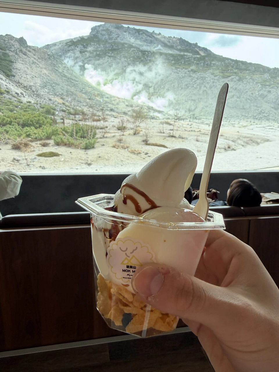 窓の外の硫黄山を背に持った、カップ入りのソフトクリーム