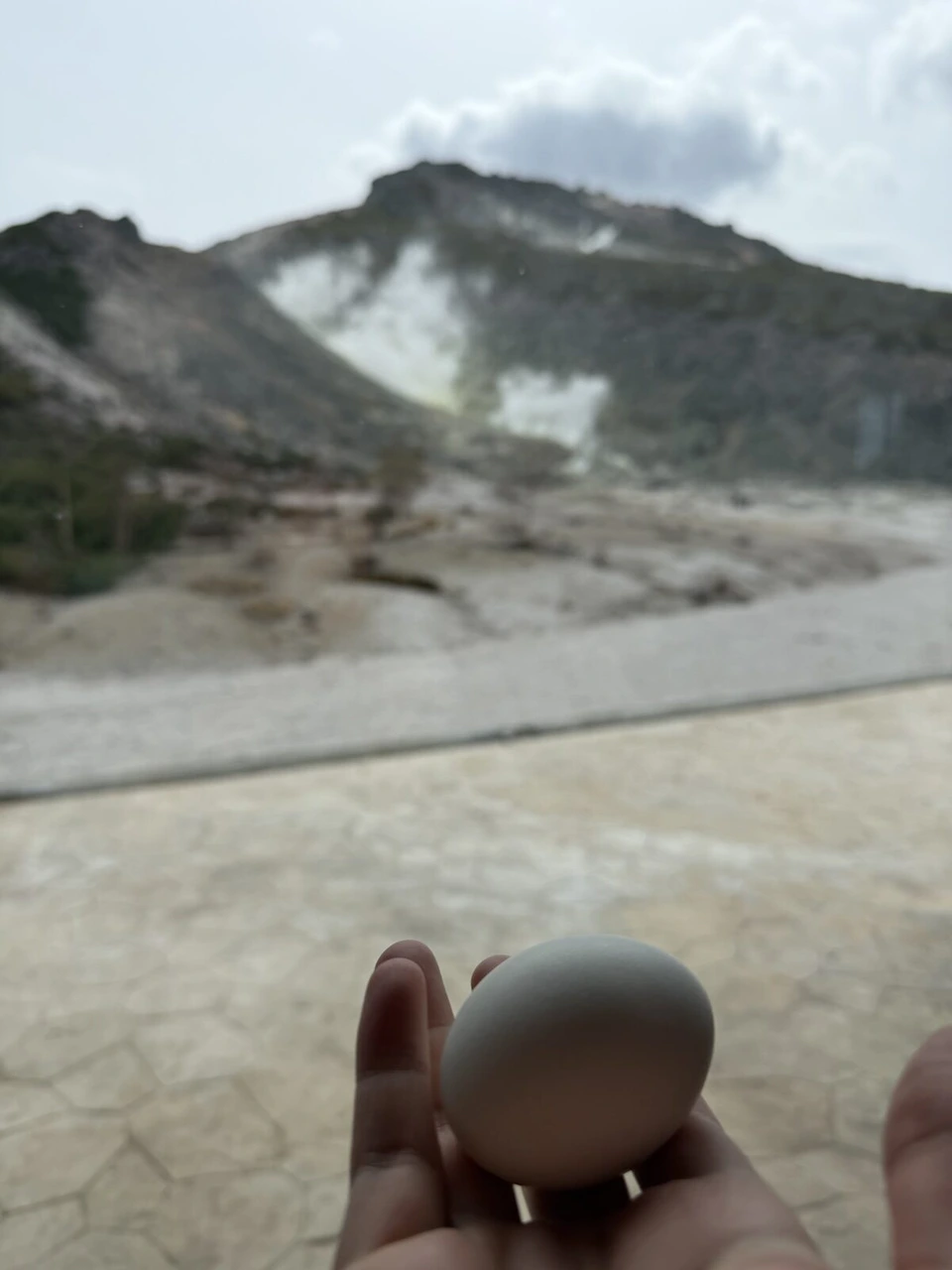 硫黄山MOKMOKベースで手のひらにのせた温泉たまごと、ぼやけた硫黄山