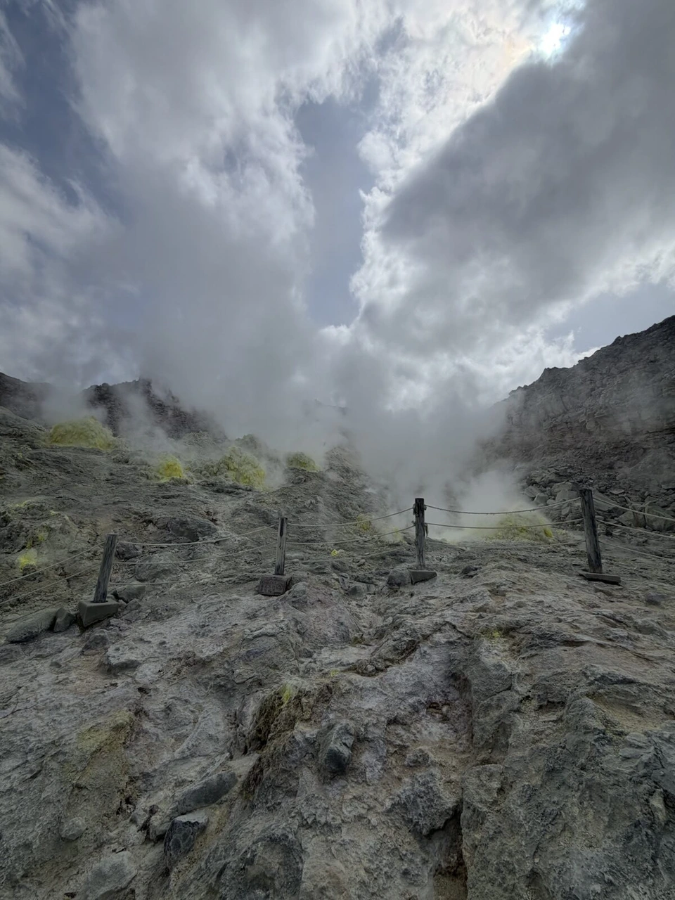 硫黄山のロープの柵が続く岩場と、その奥の噴気