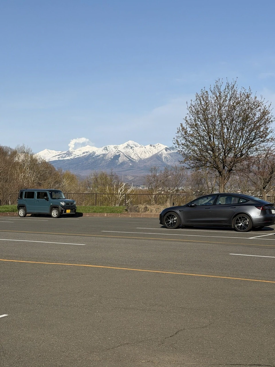 富良野・清水山の駐車場に停まった車と、その奥の十勝岳連峰と青空
