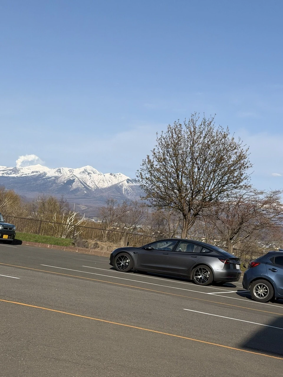 富良野・清水山の駐車場の先に見える雪をかぶった十勝岳連峰。左の山から白い噴煙が上がっている