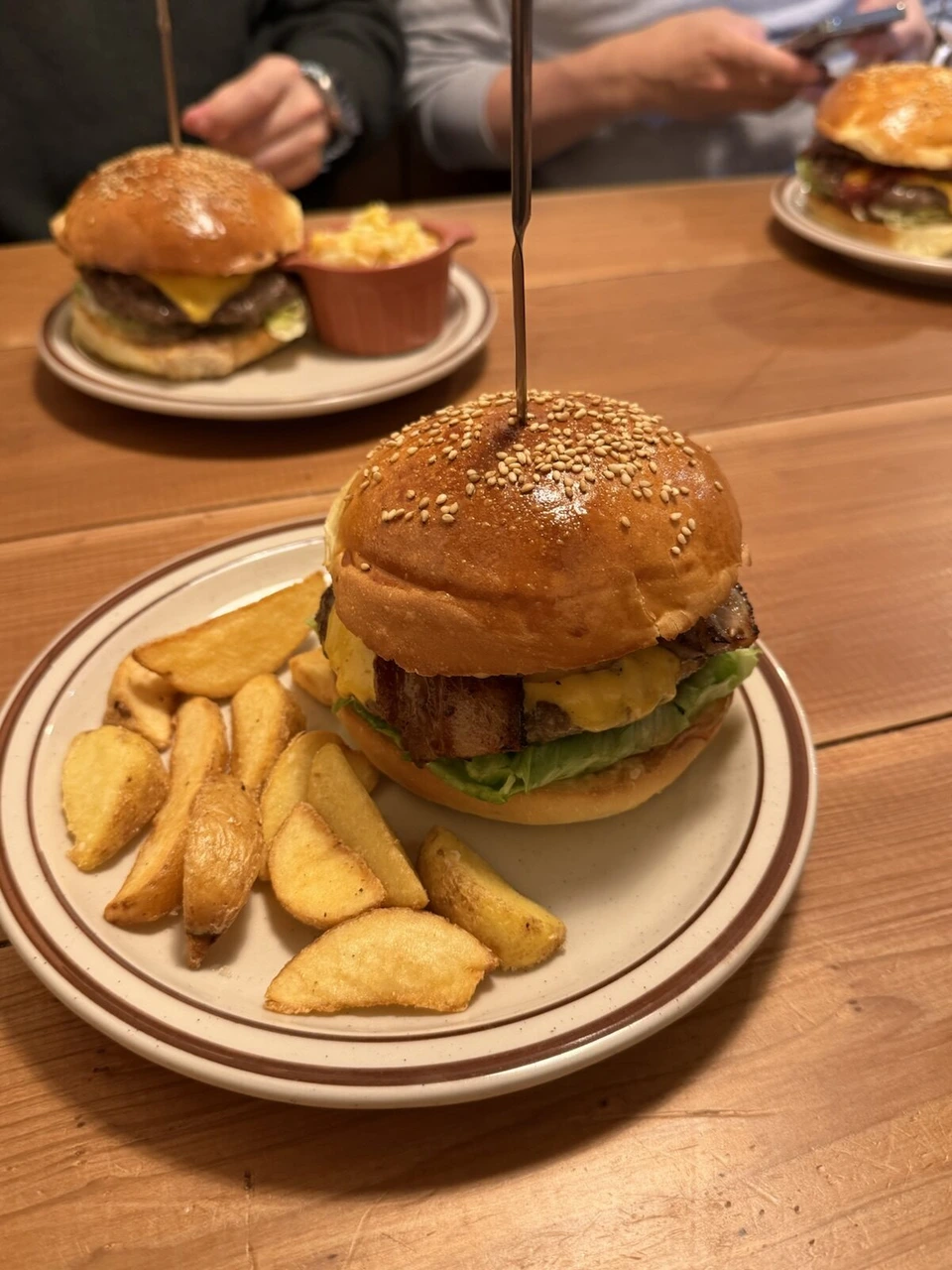 串が刺さった背の高いハンバーガーと、奥のテーブルのチーズバーガー