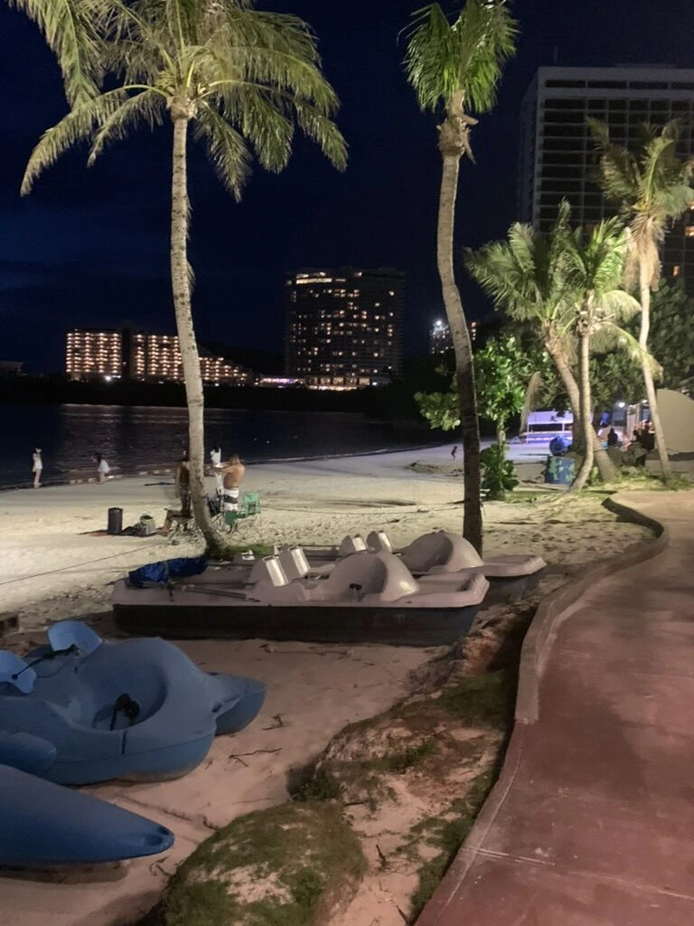 夜のタモン湾沿いの遊歩道。ライトアップされたヤシの木とビーチチェア