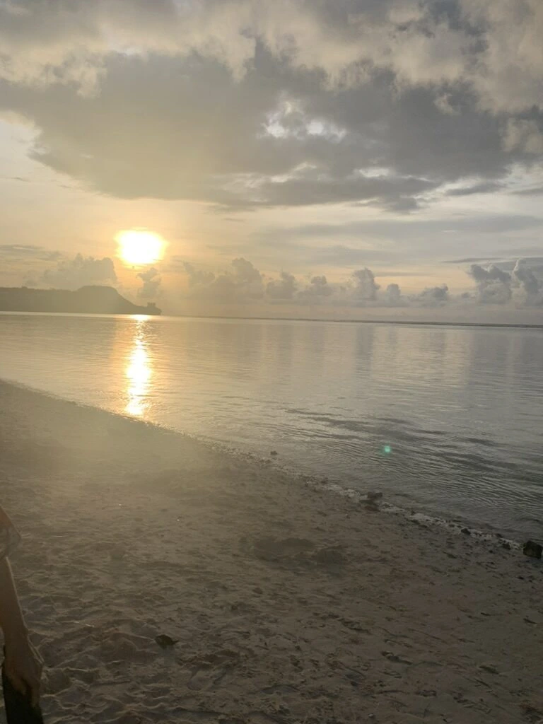 タモン湾の対岸の浜から見た、雲の間から海に沈む夕日