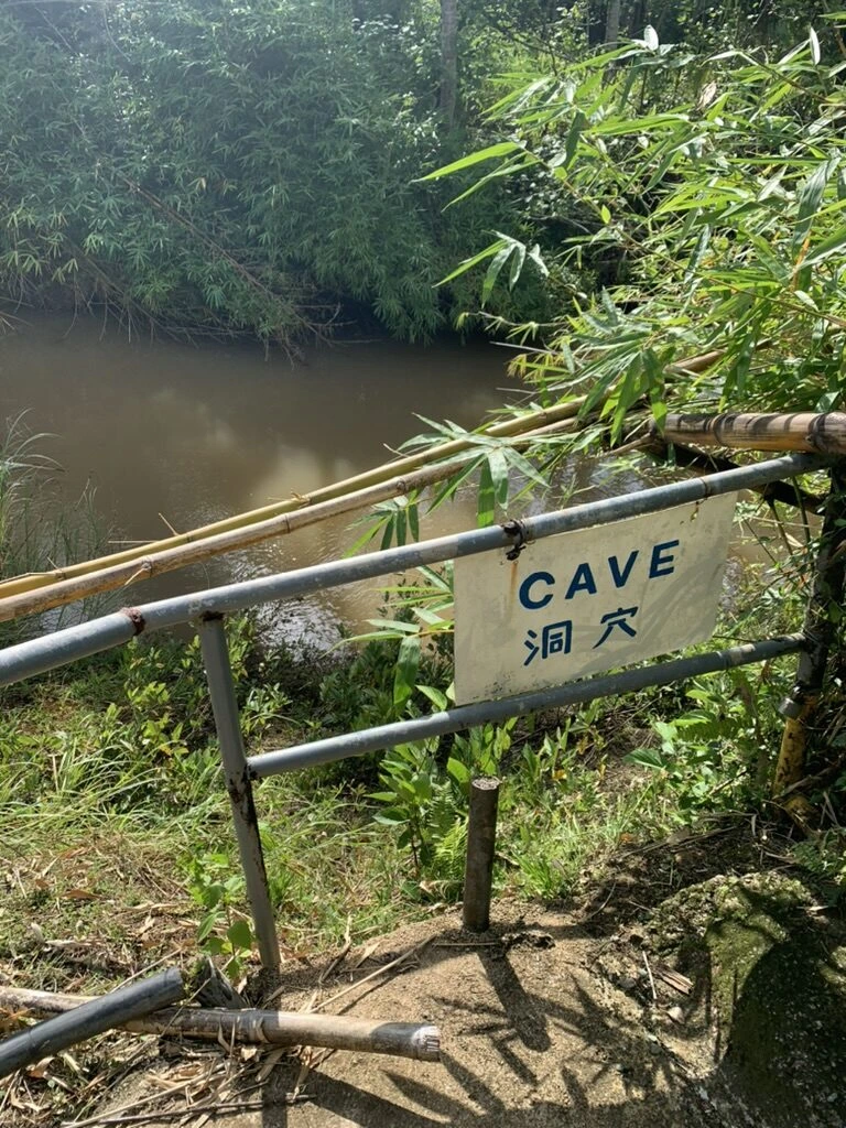 タロフォフォの滝の園内、竹の手すりの横に立つCAVE 洞穴の案内板