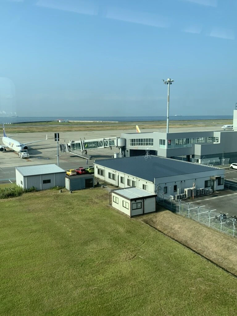 朝の神戸空港。芝生の向こうに駐機中の旅客機と管制塔