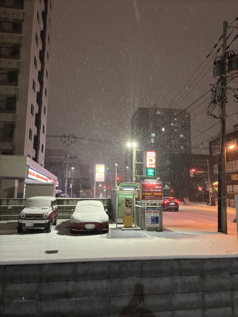 雪が強く降る札幌の夜の通り。雪をかぶった車と駐車場の看板