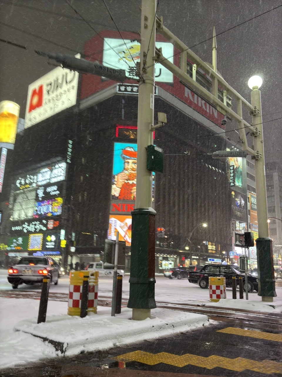 雪の夜の札幌・すすきの交差点。ビルの大きな看板と路面電車の電柱