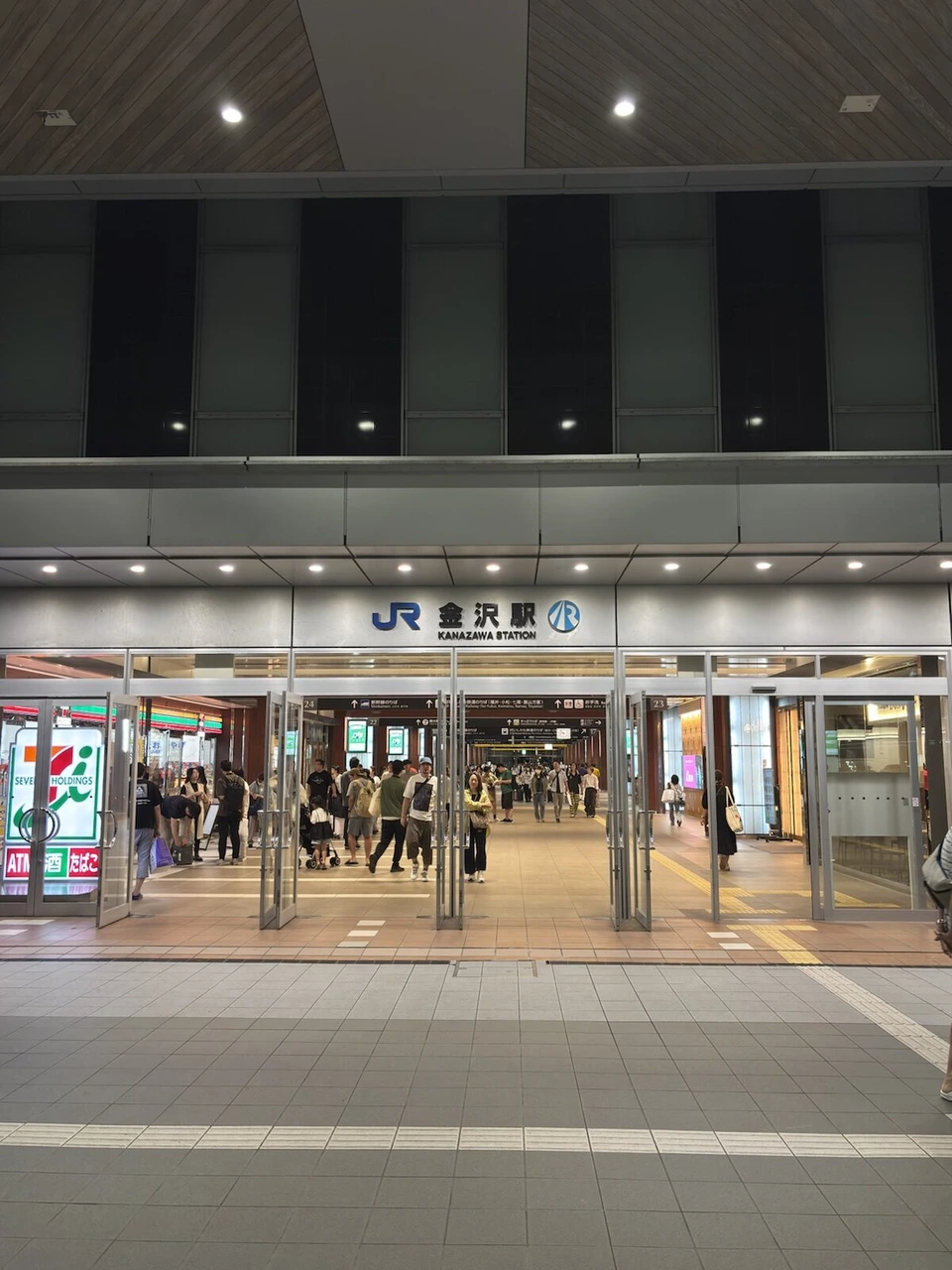夜の金沢駅の入口。JR金沢駅の看板の下を人が行き来している