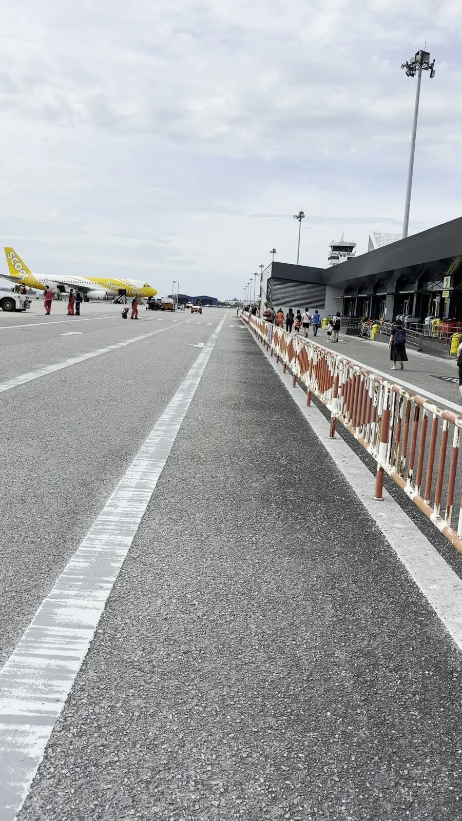 ランカウイ空港の駐機場。柵の横をターミナルへ歩く乗客、奥にスクートの黄色い機体と管制塔